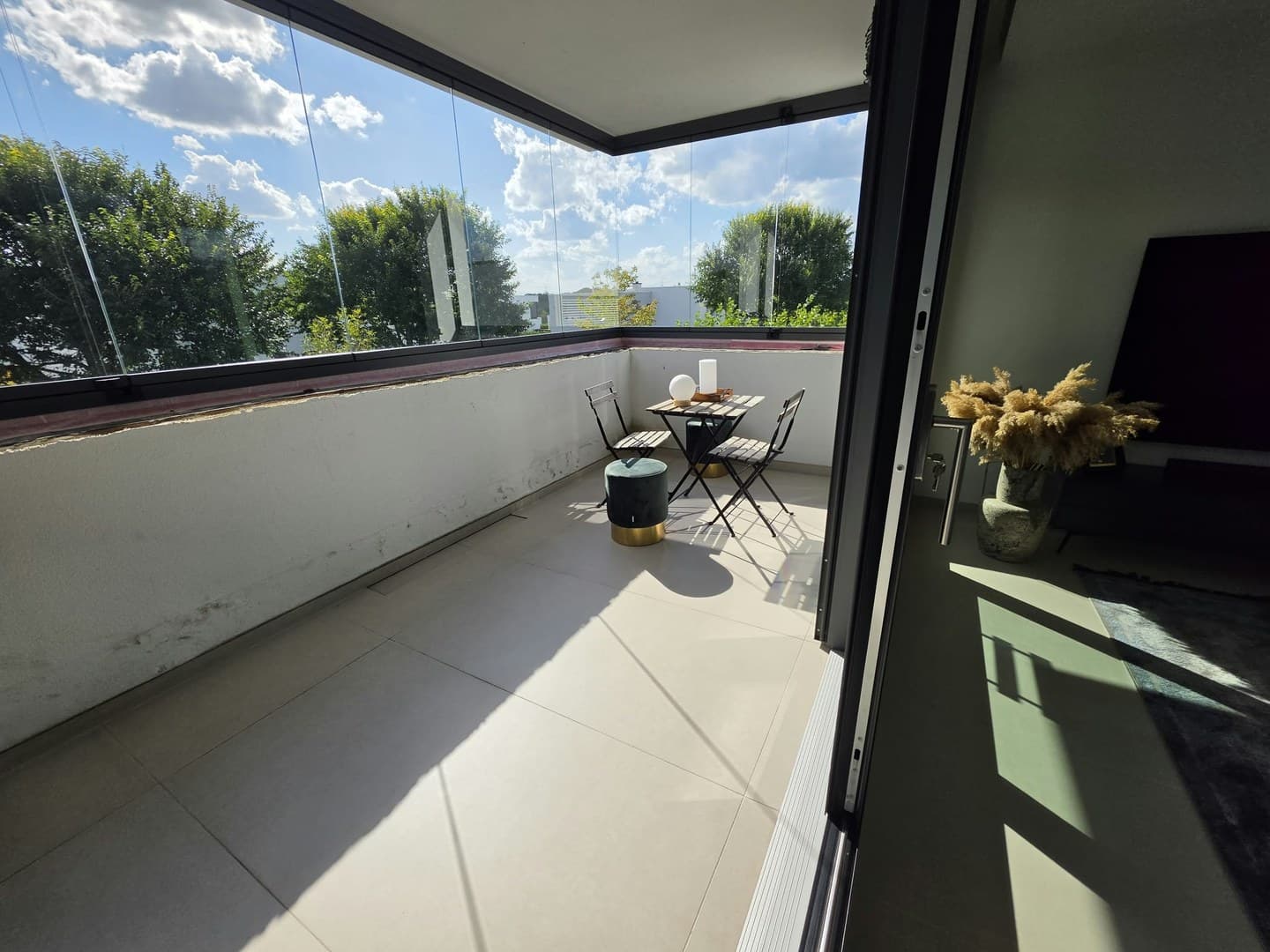 Verglaster Balkon mit hellen großformatigen Bodenfliesen in der Sonne und kleiner Sitzgruppe