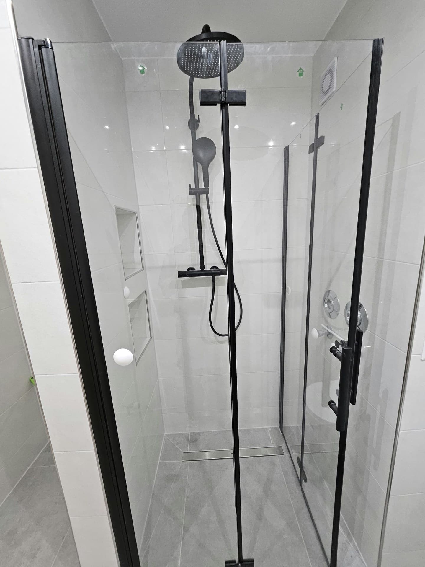 Dusche mit Regenbrause, schwarz gerahmter Glastür, zwei gefliesten Wandnischen und Duschrinne im Boden