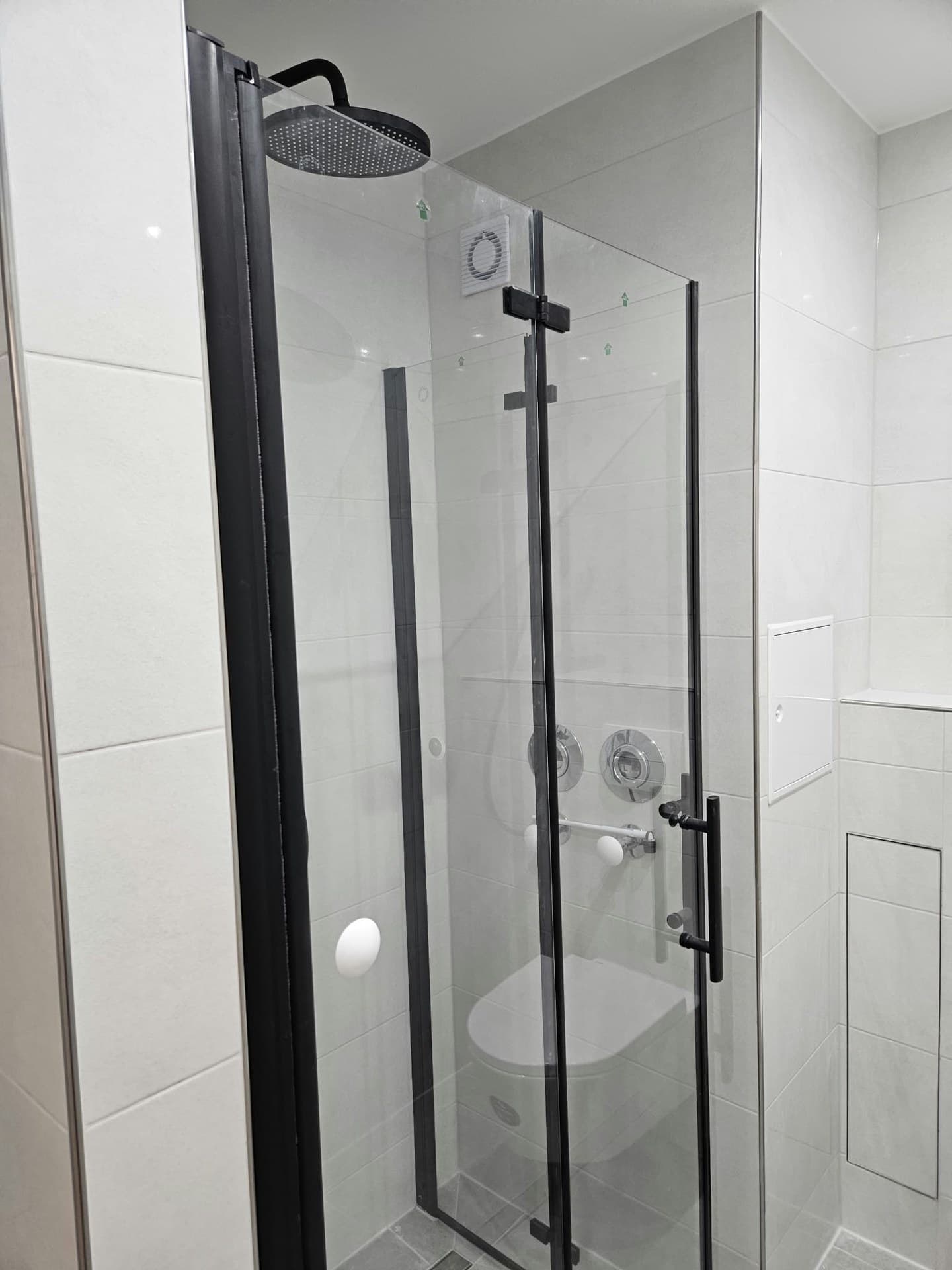 Dusche mit Glasabtrennung, schwarzen Griffen und hellen Wandfliesen