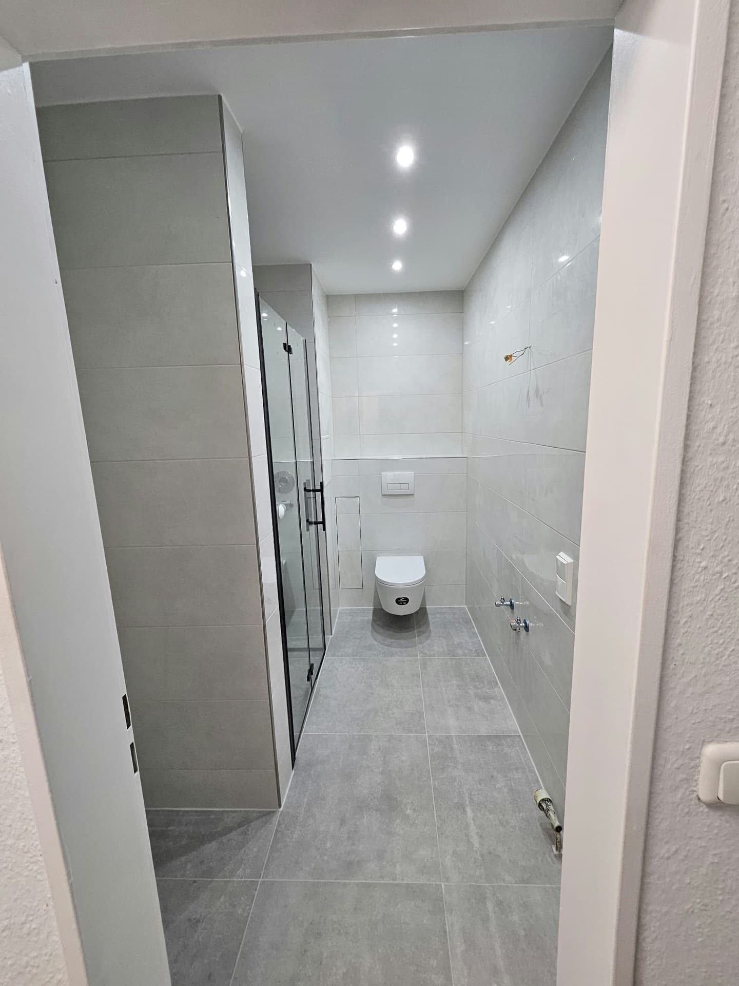 Bad mit hellgrauen Fliesen, Glasdusche und Wand-WC am Ende des Raums